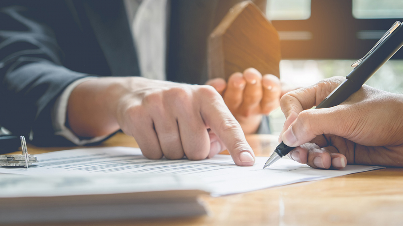 Close up of Business man pointing and signing agreement for buying house. Bank manager concept.